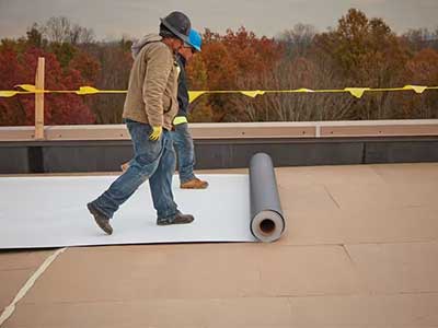Two workers rolling out a white, single-ply sheet on a commercial roof